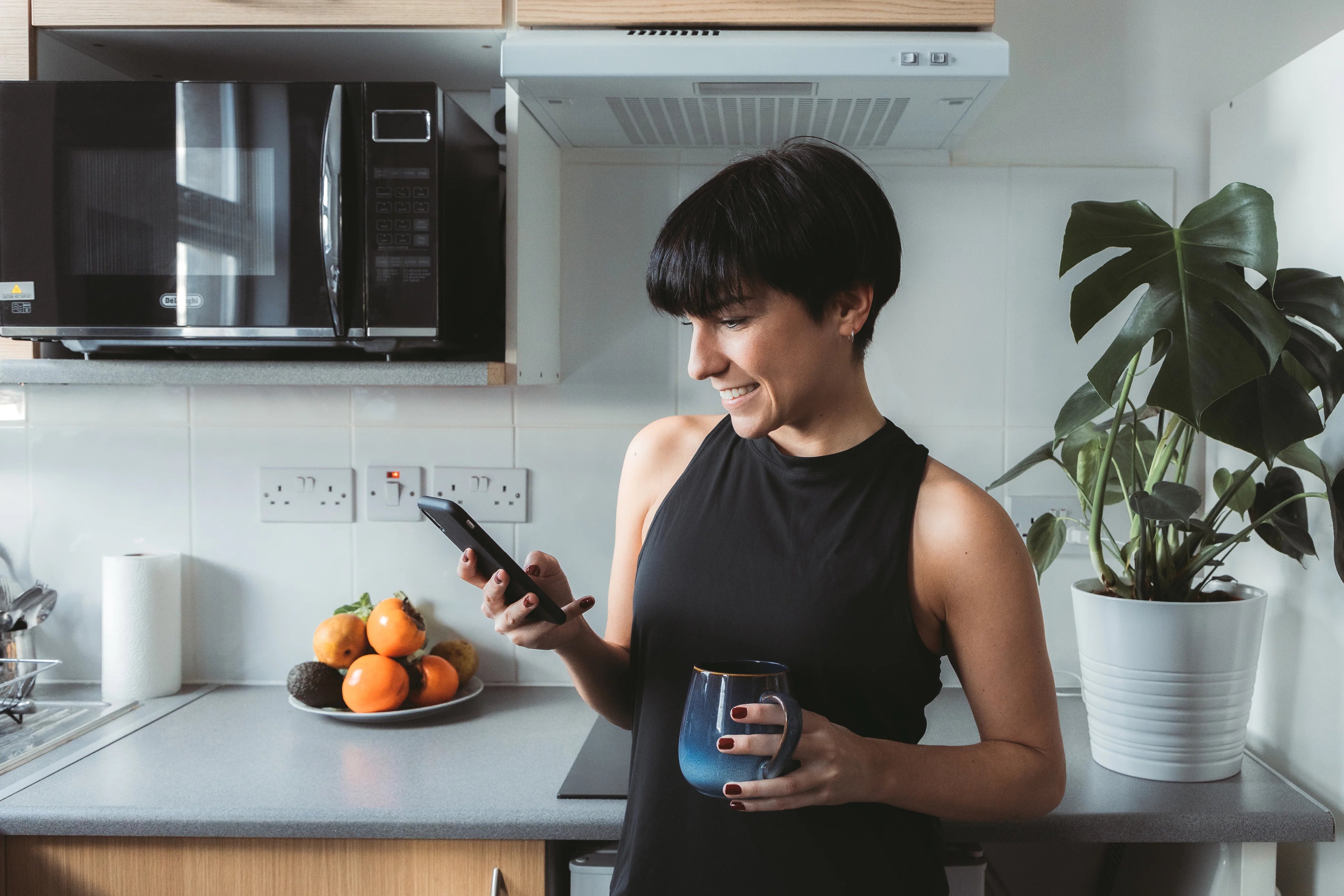 files/woman-stands-in-the-kitchen-and-smiles-while-using-cell-phone.webp